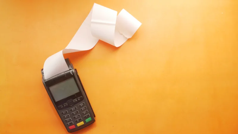 Card payment terminal printing a long paper receipt on an orange surface