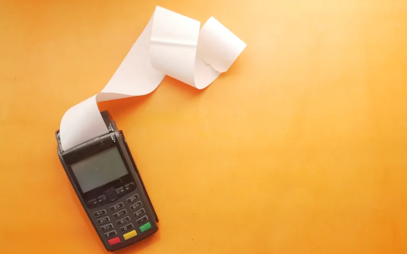 Card payment terminal printing a long paper receipt on an orange surface