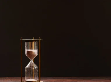 Brass hourglass on a dark table, a stand-in for the install delay that stops a malicious Claude Code extension