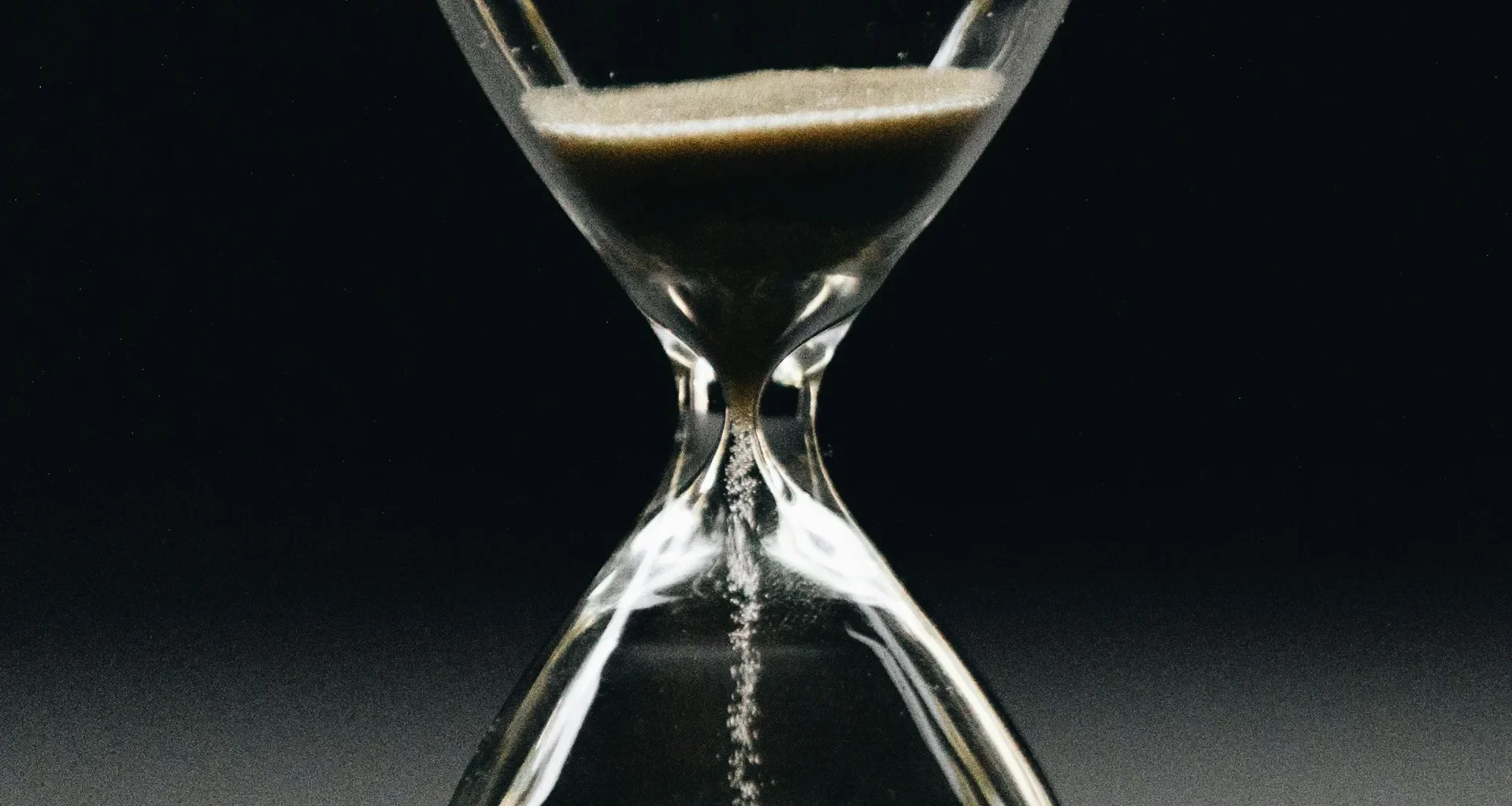 A clear glass hourglass with sand running from the upper bulb to the lower