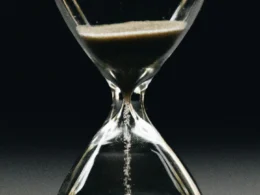 A clear glass hourglass with sand running from the upper bulb to the lower