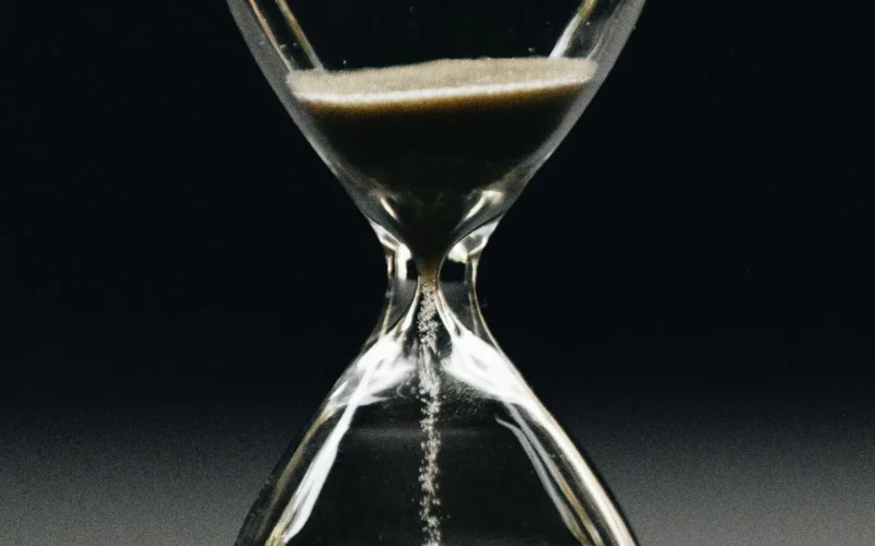 A clear glass hourglass with sand running from the upper bulb to the lower