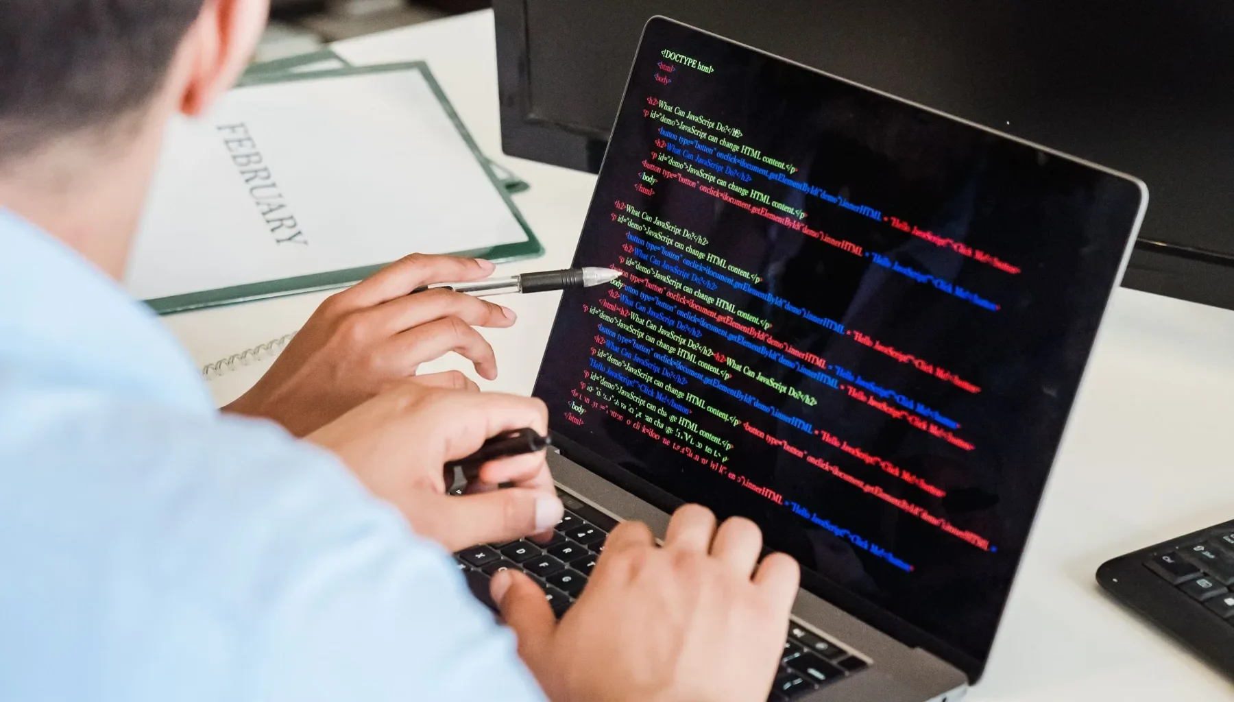 Developer typing colour-coded code on a laptop at an office desk.