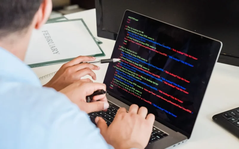 Developer typing colour-coded code on a laptop at an office desk.