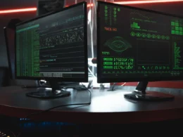 Two monitors showing green code in a dark room, where secret scanning checks every commit