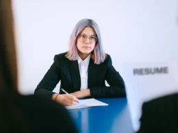 Young job candidate in a suit taking notes across from an interviewer holding a resume.
