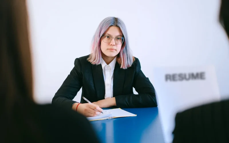 Young job candidate in a suit taking notes across from an interviewer holding a resume.