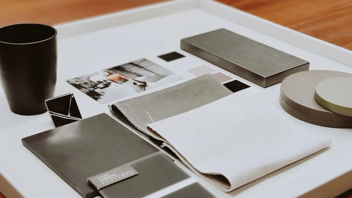 Fabric, metal and stone material samples arranged on a white tray on a wooden desk