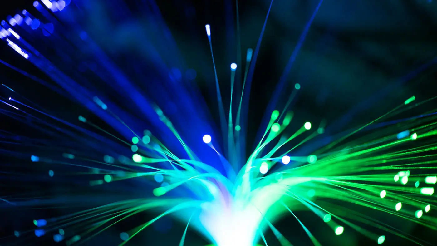 Close-up of glowing blue and green fibre optic strands spreading out from a single bright point