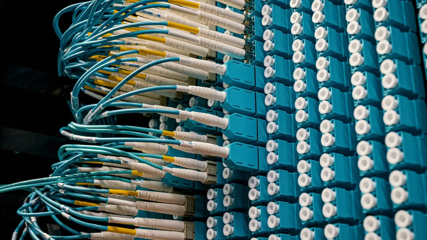 Blue fibre patch cables plugged into rows of ports on a data centre patch panel