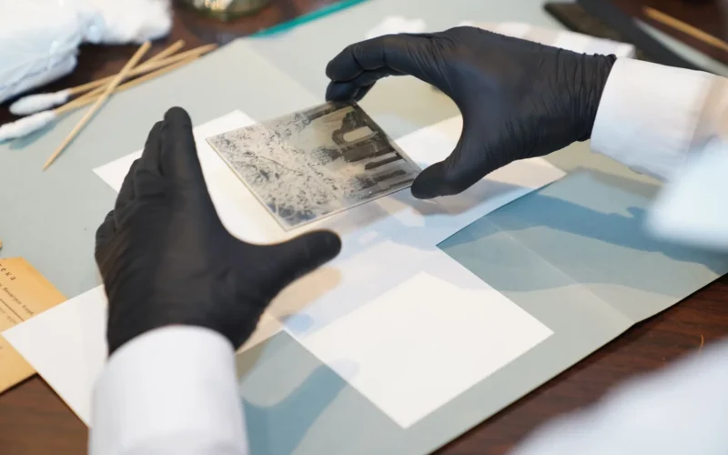 Gloved hands holding an old glass photo negative during restoration, the kind of family archive FOLKLY.ai sets out to preserve