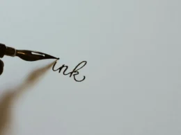 A hand holding a black fountain pen and writing on white paper