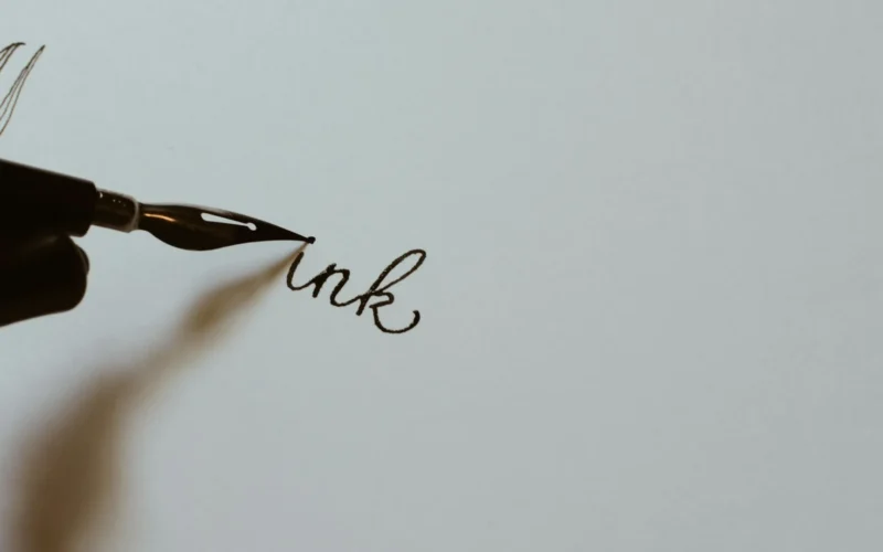 A hand holding a black fountain pen and writing on white paper