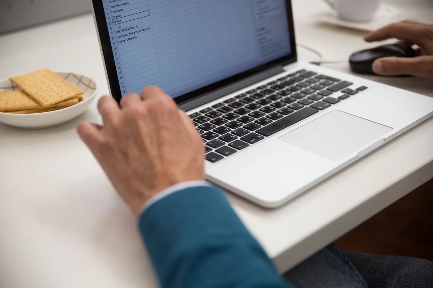Man in a suit working on a laptop at a white desk.