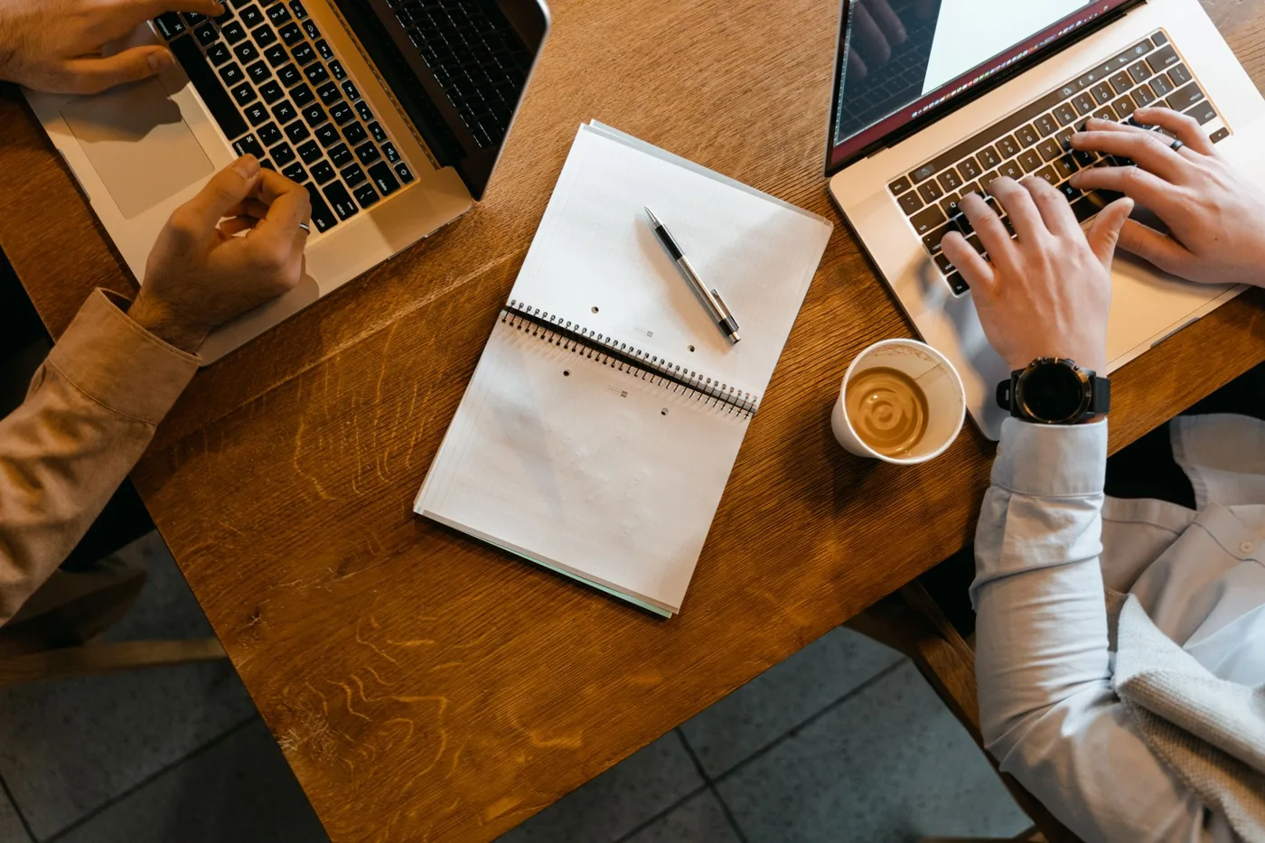Haiku 5.5 vs GPT-6 Luna: two coworkers working side by side on laptops at a wooden desk with notes and coffee.
