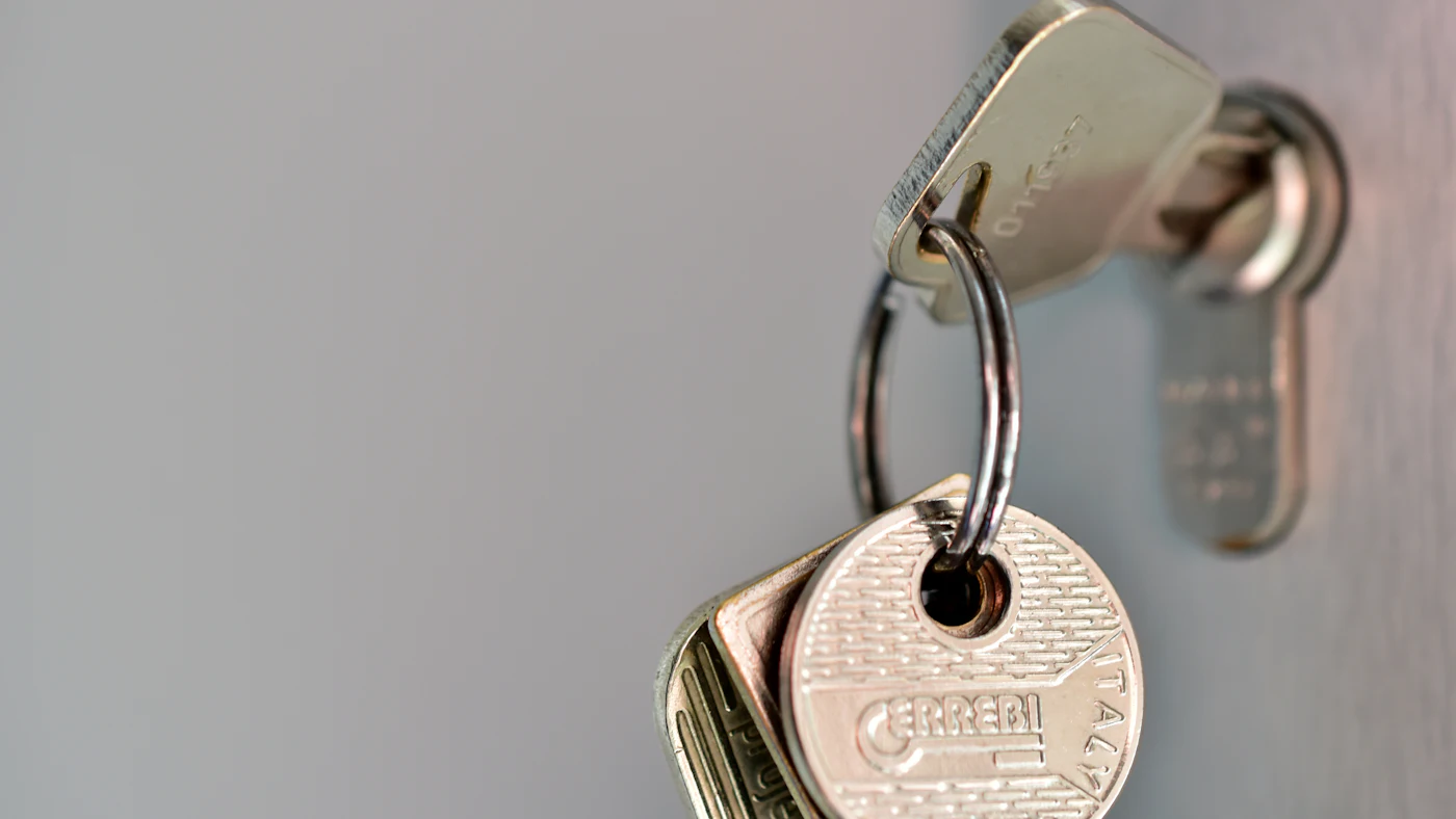 Ring of keys left in a door lock cylinder against a pale grey wall