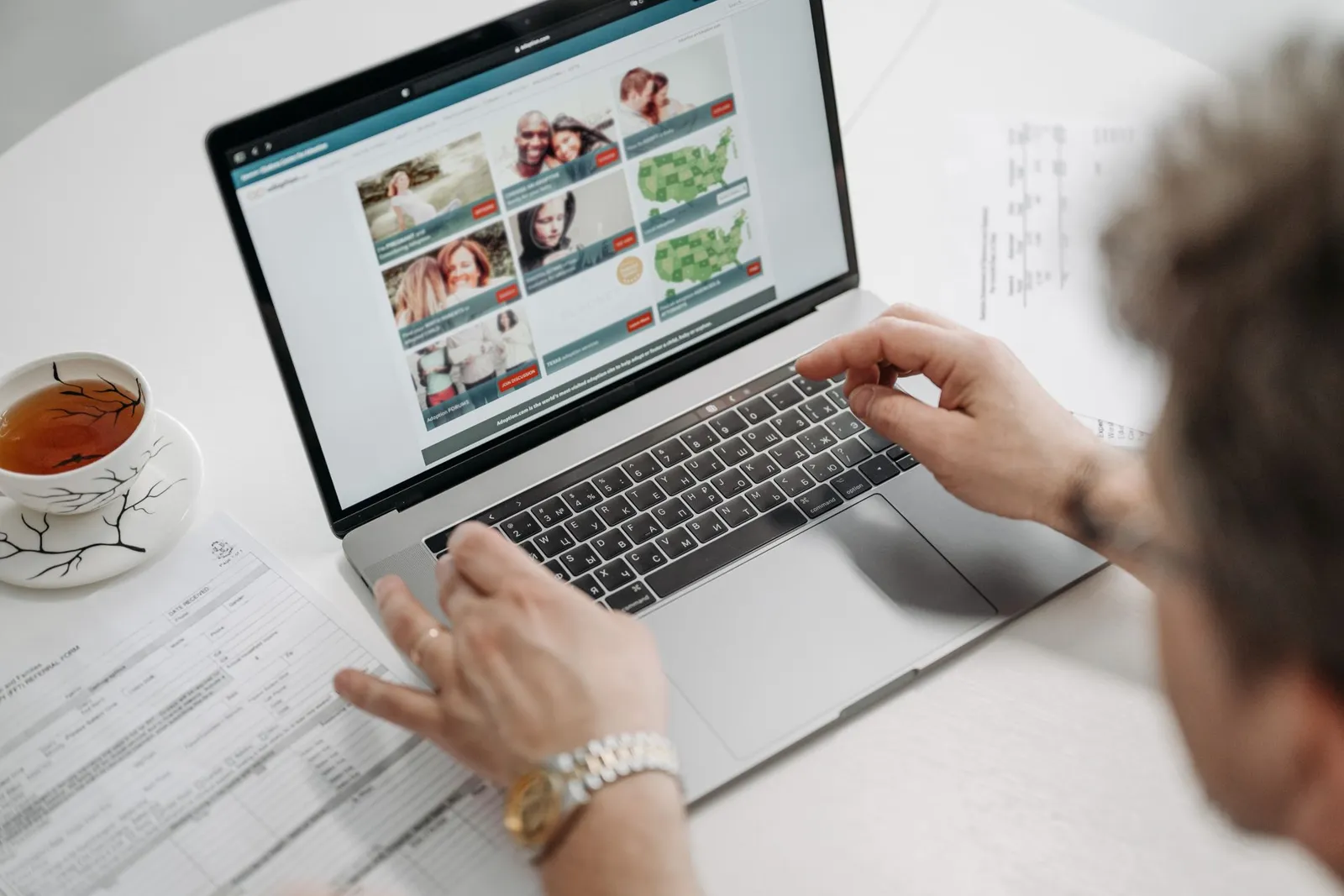 Person browsing a website on a laptop beside paper documents and tea, a reminder to set Gemini in Chrome tab sharing