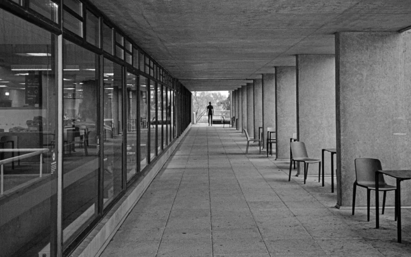 Long concrete walkway with windows and a distant person