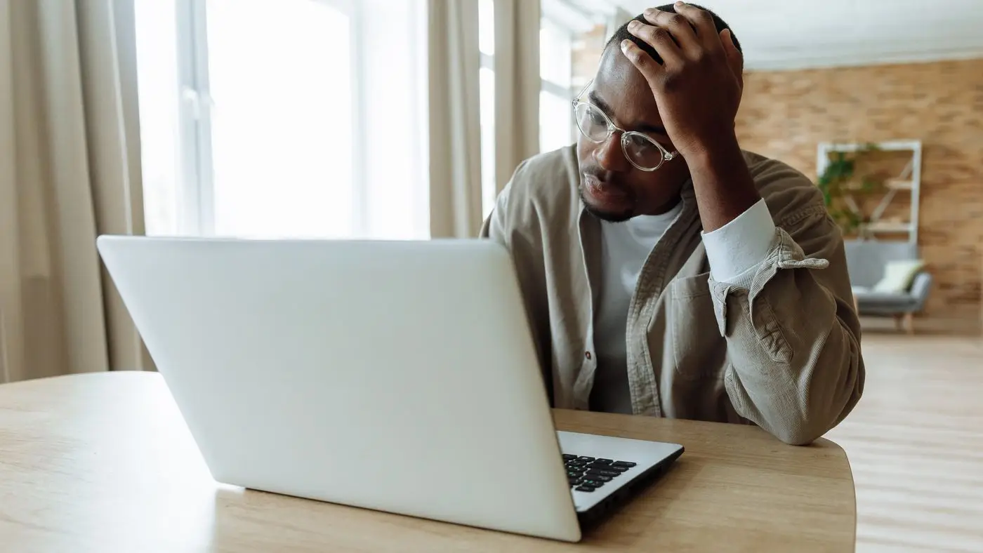 Man with glasses holding his head while looking at a laptop, the moment an AI outage plan is needed