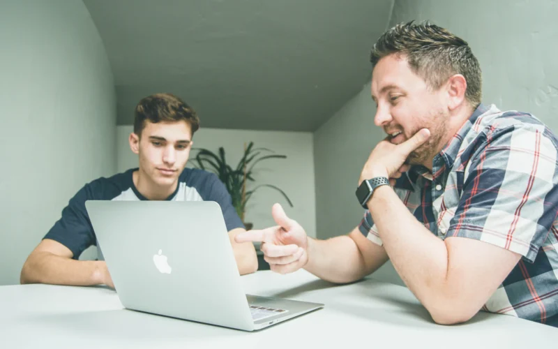 Two colleagues talking across a desk with a laptop in a bright office