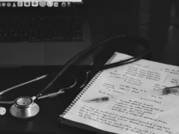 A notebook with a stethoscope resting on it beside a laptop