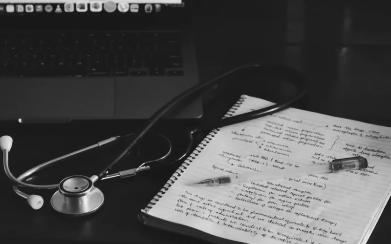 A notebook with a stethoscope resting on it beside a laptop