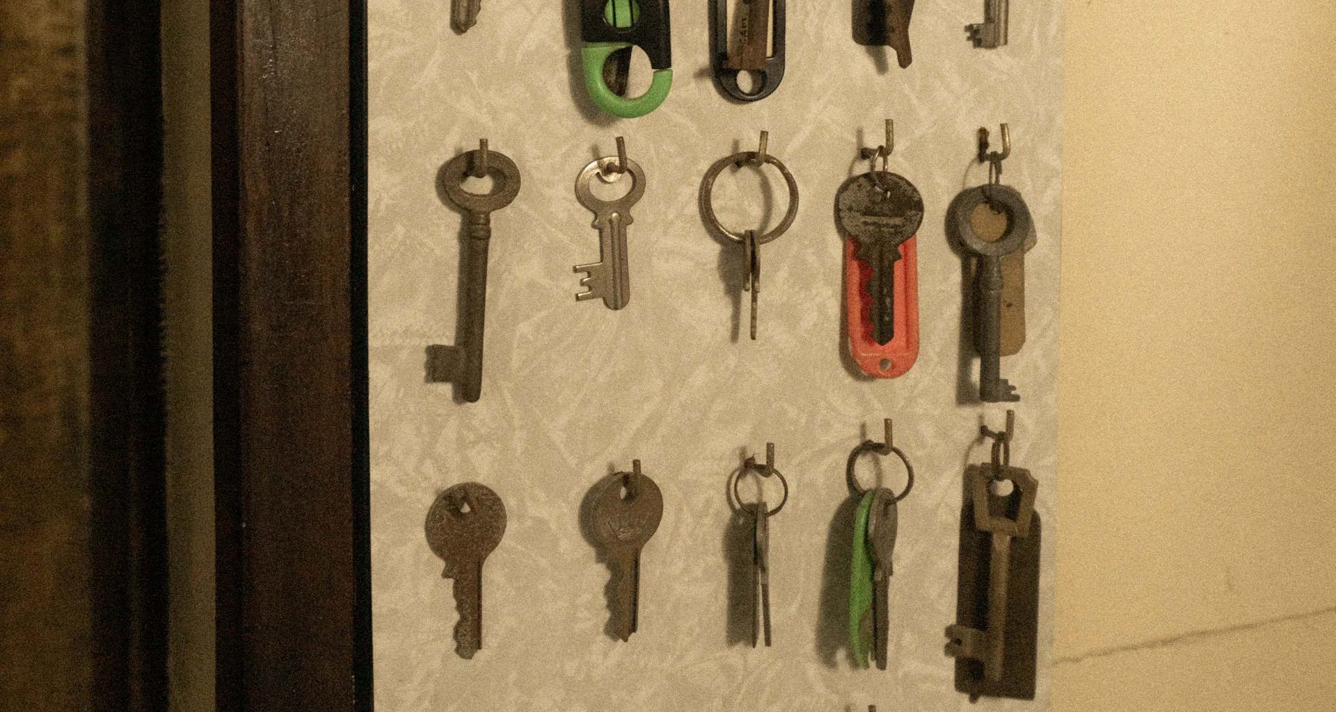 Rows of old metal keys hanging from hooks on a pale patterned wall