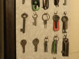 Rows of old metal keys hanging from hooks on a pale patterned wall.