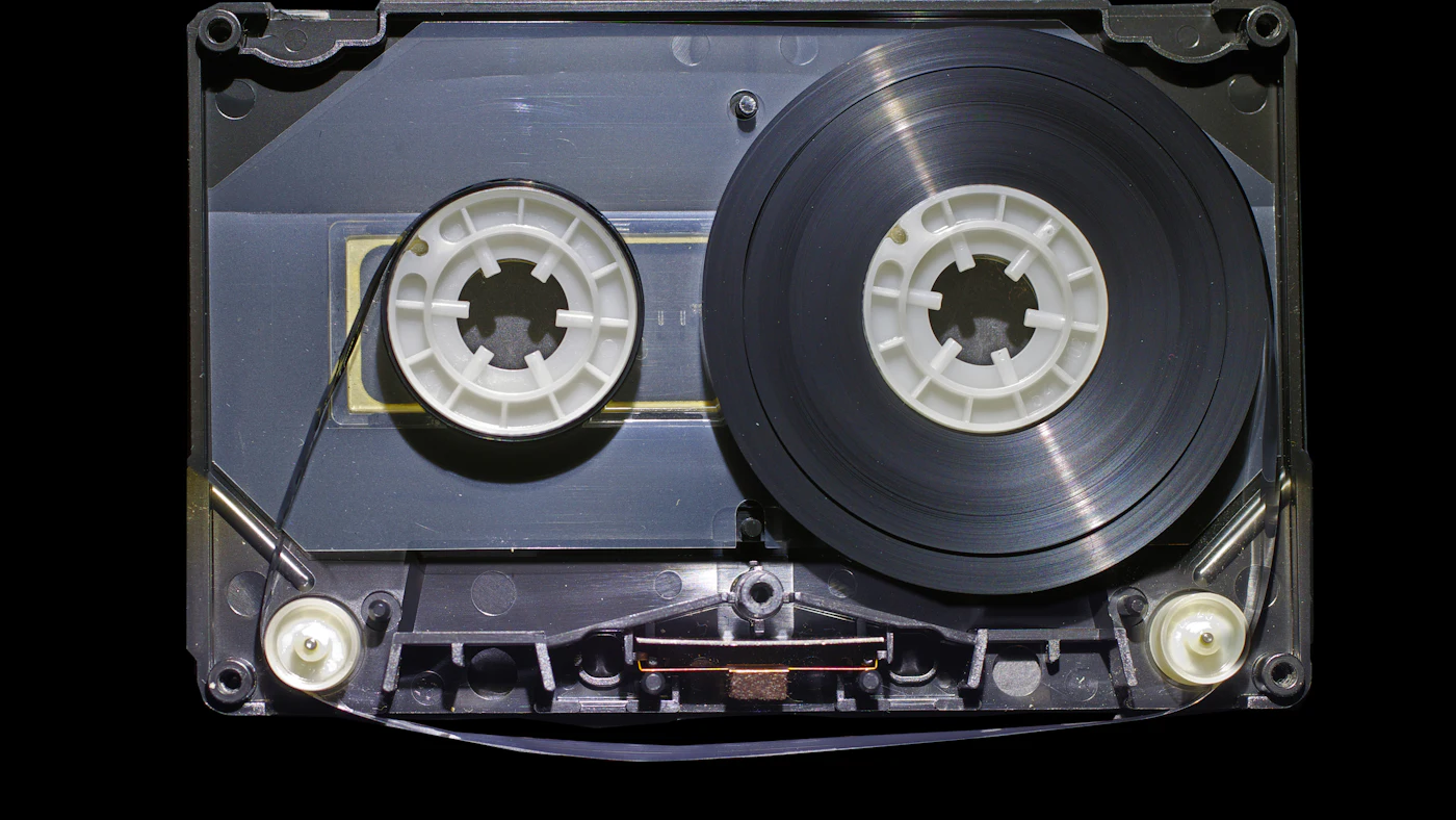Open audio cassette showing its tape reels against a black background