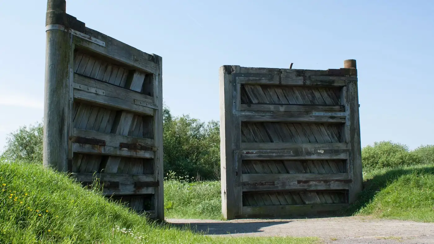 Two weathered wooden gates standing open on a gravel path between grassy banks under a blue sky