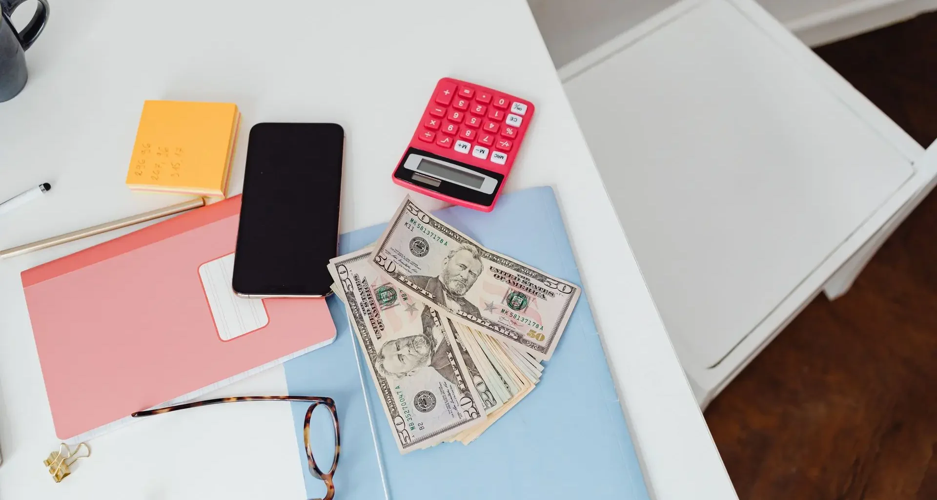 Calculator, banknotes, notebook and phone on a white desk, ready to check Fable 5.1 pricing against a budget