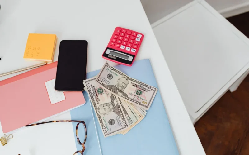 Calculator, banknotes, notebook and phone on a white desk, ready to check Fable 5.1 pricing against a budget