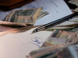 A pen and scattered banknotes resting on printed financial documents