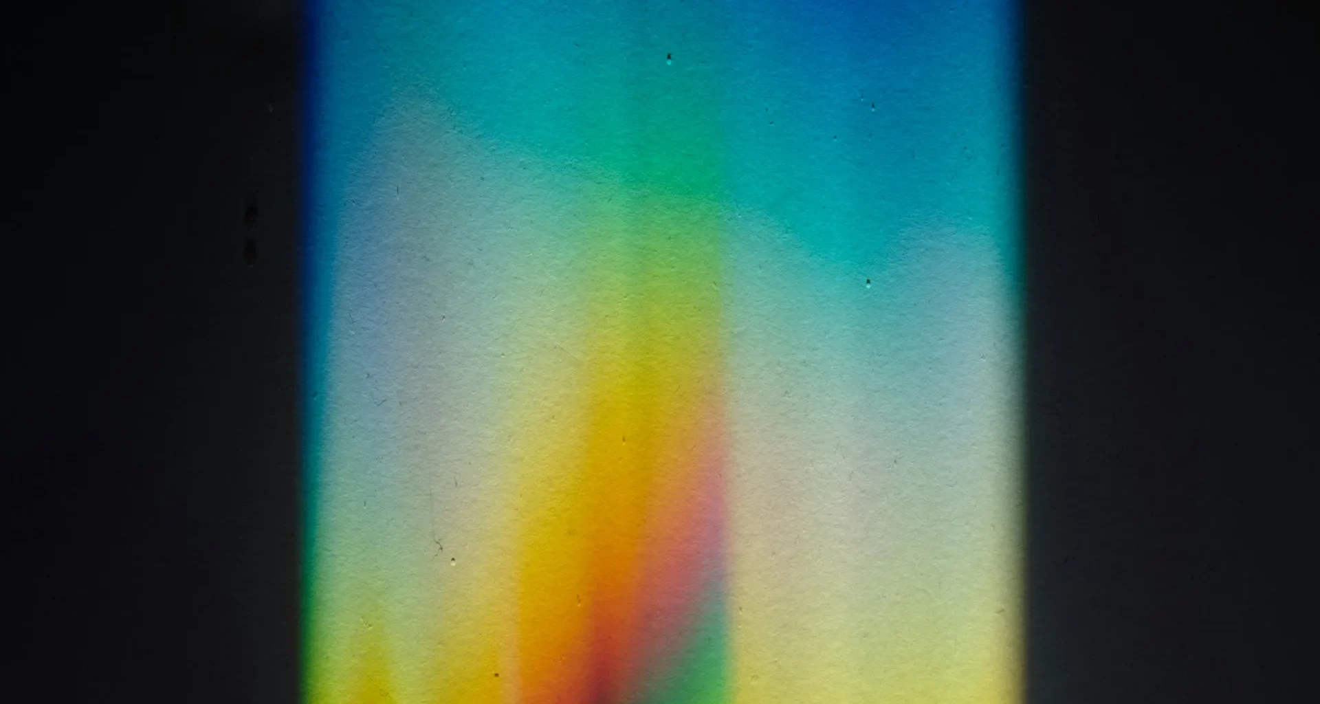 A beam of light splitting into a rainbow spectrum through a prism on a black surface