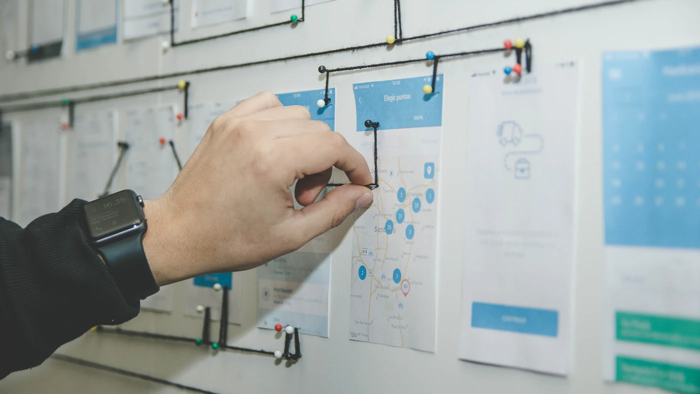 Hand pointing at a process map of paper cards pinned to an office wall