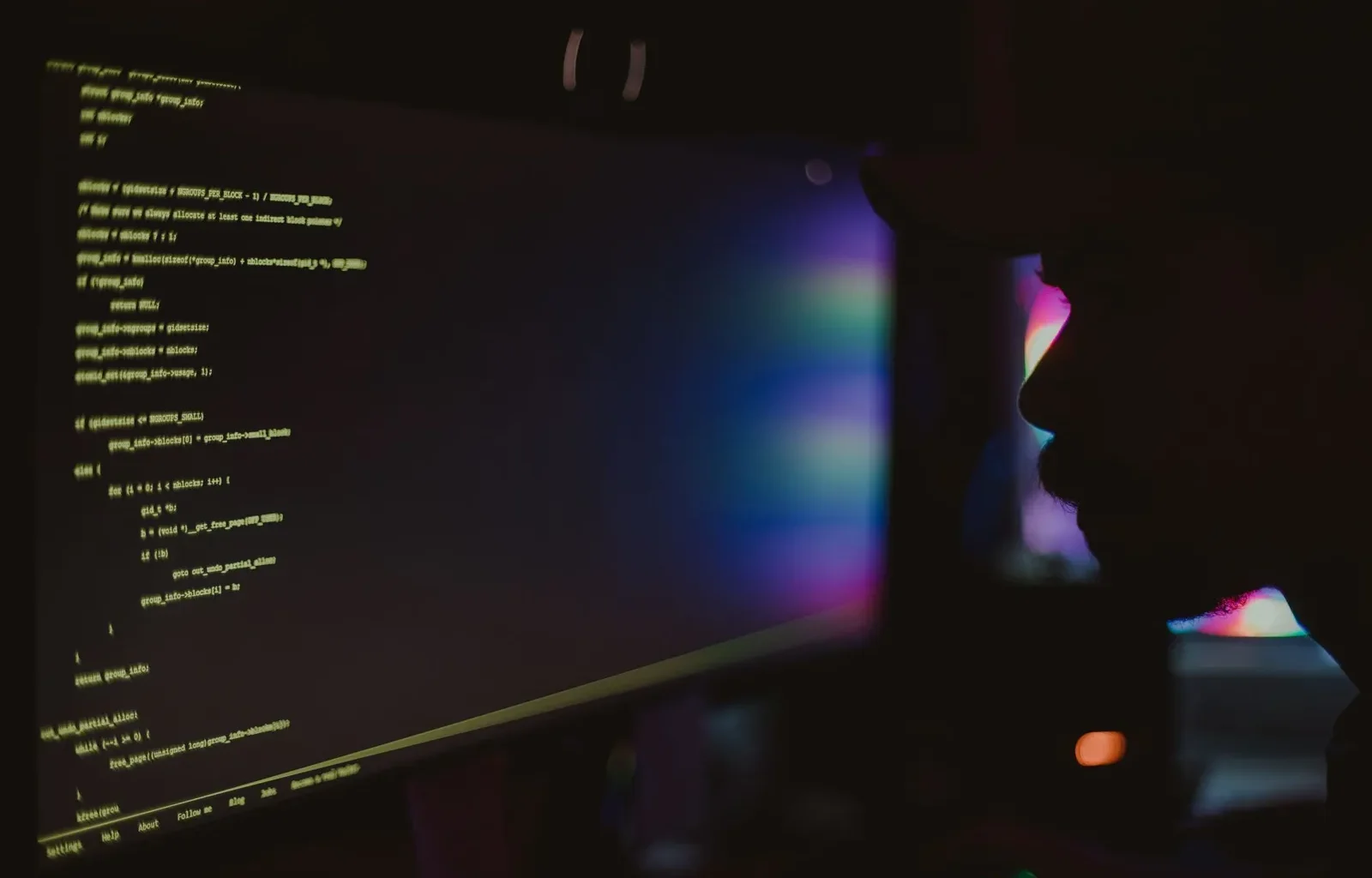 Silhouette of a programmer in a dark room facing a monitor full of code.