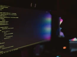 Silhouette of a programmer in a dark room facing a monitor full of code.