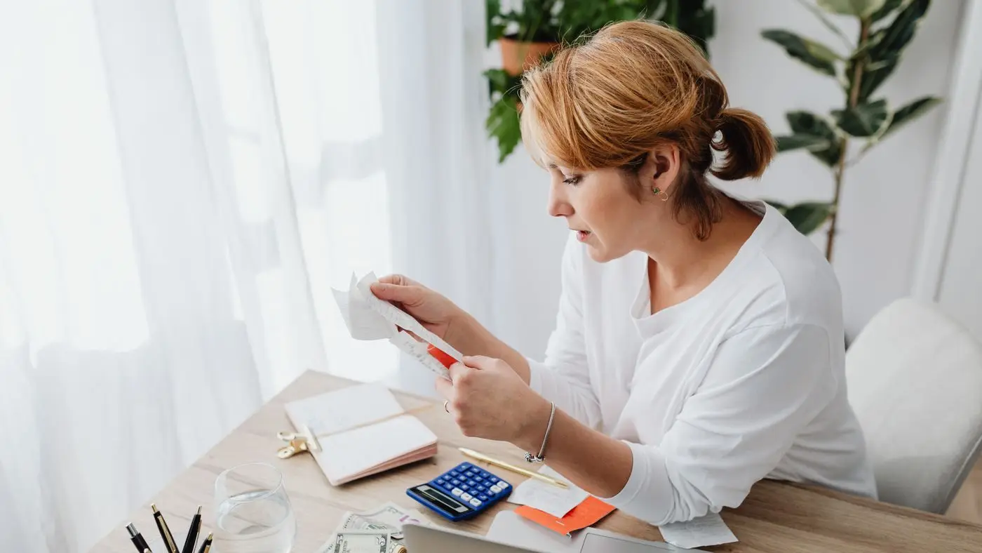 Fable 5.1 pricing: woman at a wooden desk reading a paper receipt beside a blue calculator.