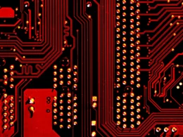 A red and black circuit board with metallic pathways and solder points