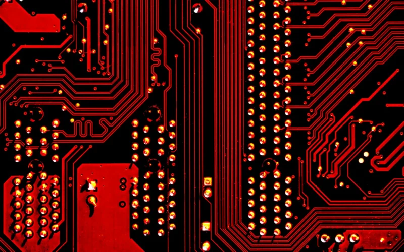 A red and black circuit board with metallic pathways and solder points