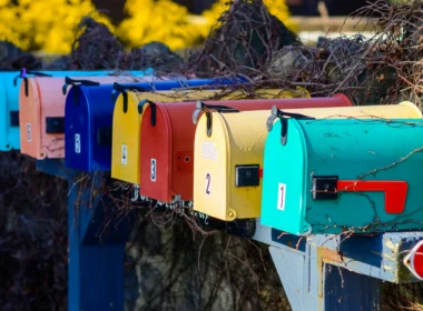 A row of colourful mailboxes beside a bush