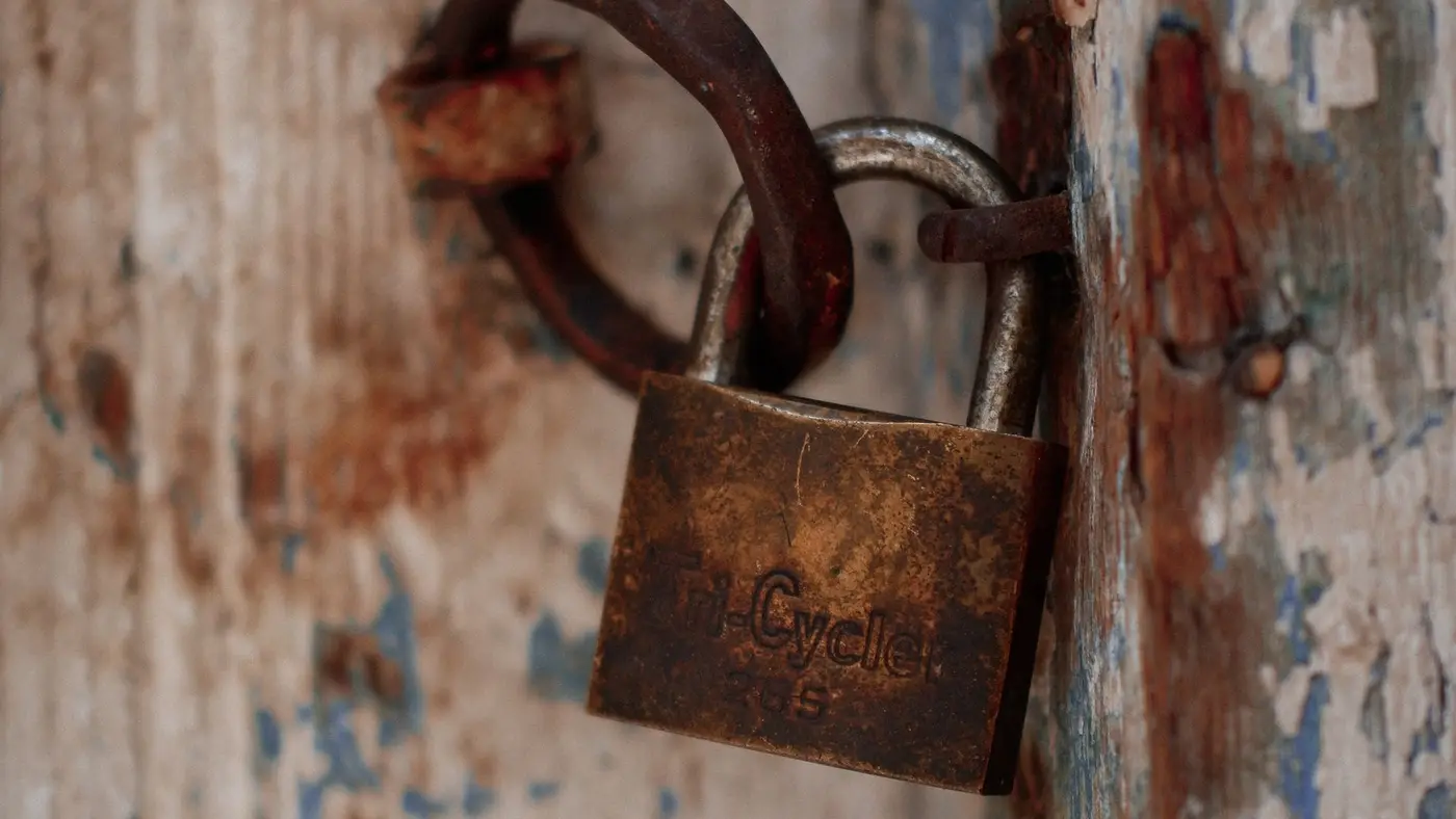 Rusty padlock hanging from a weathered wooden door with peeling blue and white paint