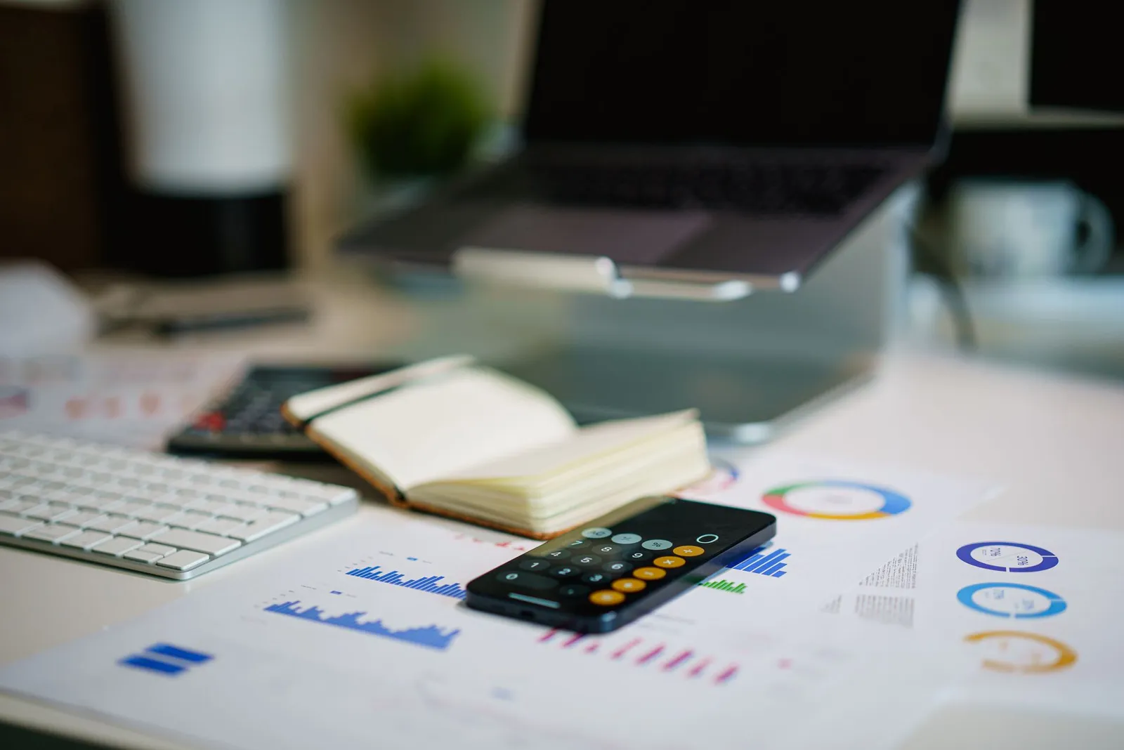 Smartphone calculator on a desk beside printed charts and a laptop, for working out an AI agent token budget