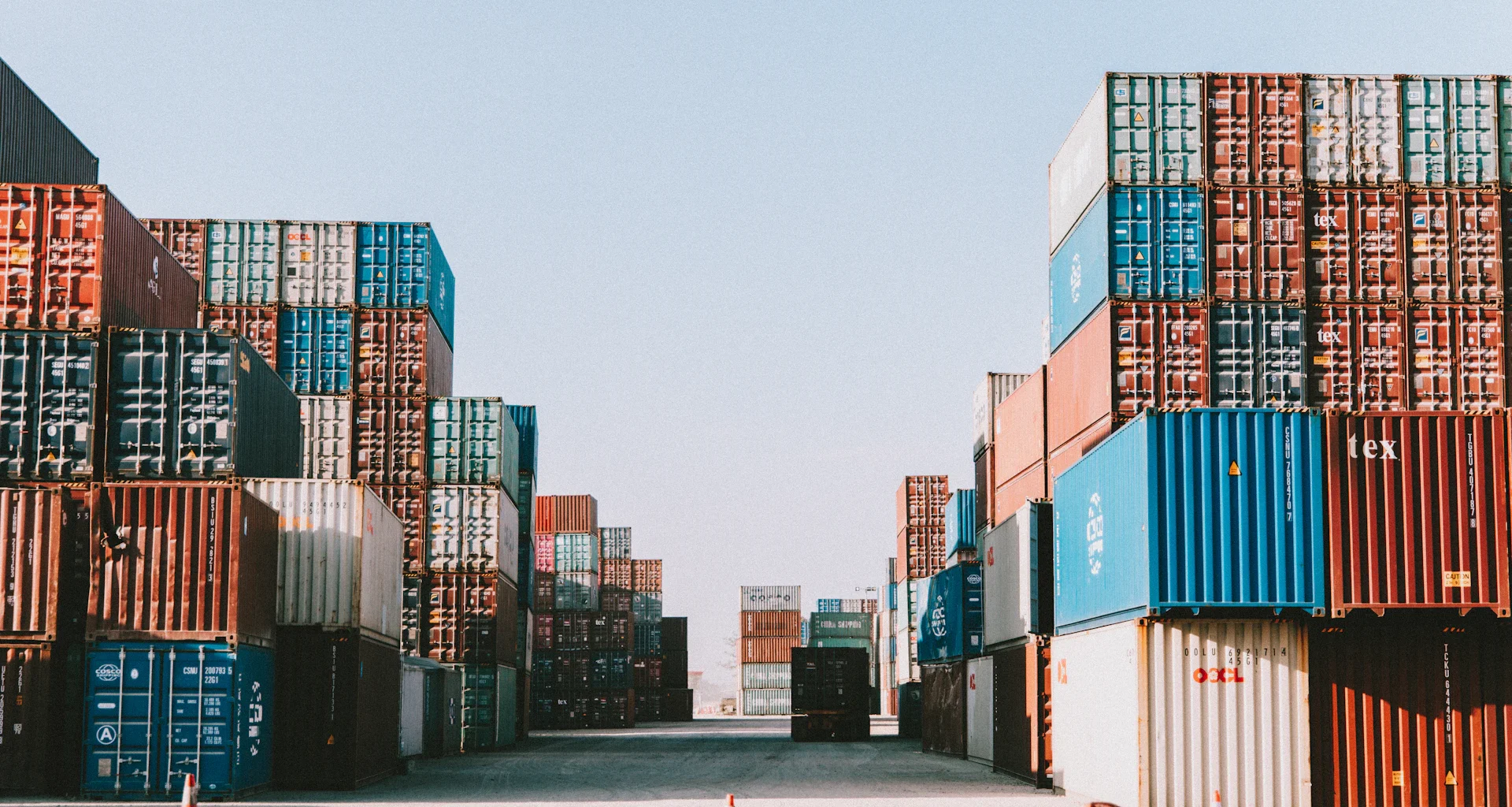 Stacks of shipping containers lining a port yard under a clear sky