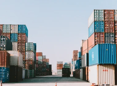 Stacks of shipping containers lining a port yard under a clear sky