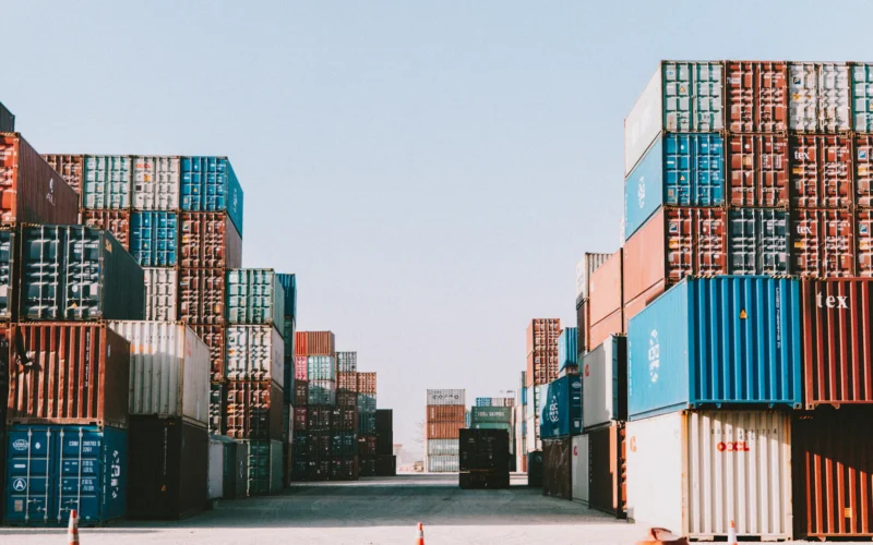Stacks of shipping containers lining a port yard under a clear sky