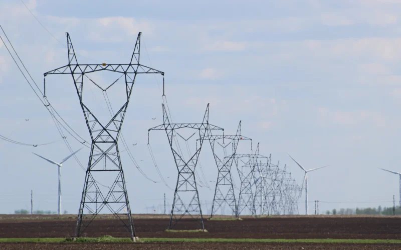 Row of high-voltage transmission towers crossing flat farmland under a pale sky