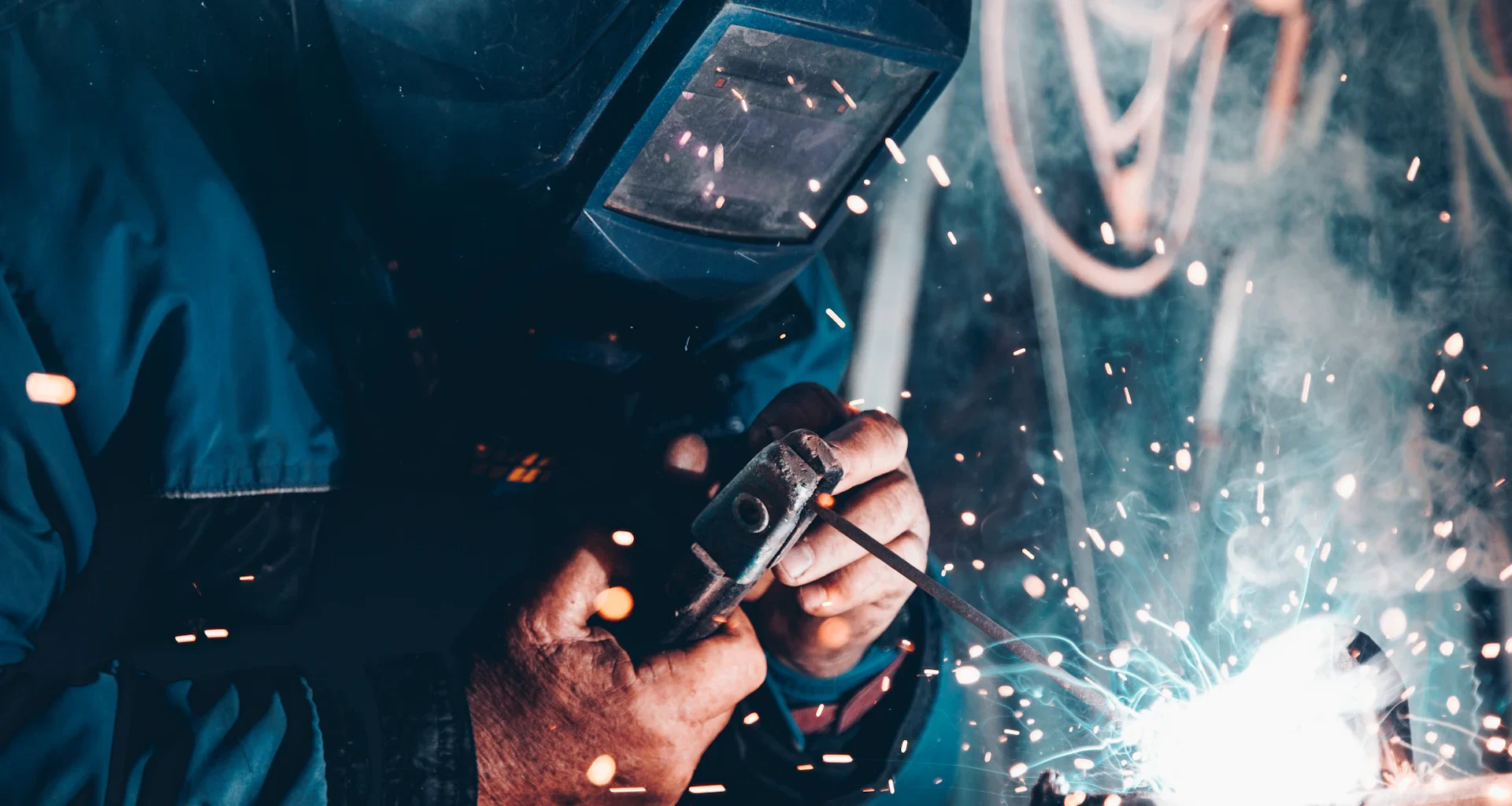 Welder in a protective mask working on metal as sparks fly