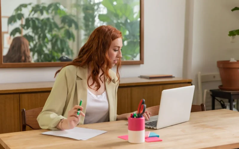 Woman working at a laptop with documents in a bright office, where Gemini in Chrome could read the open tab