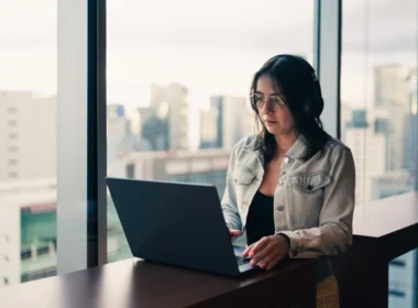 Woman wearing headphones working on a laptop by a window